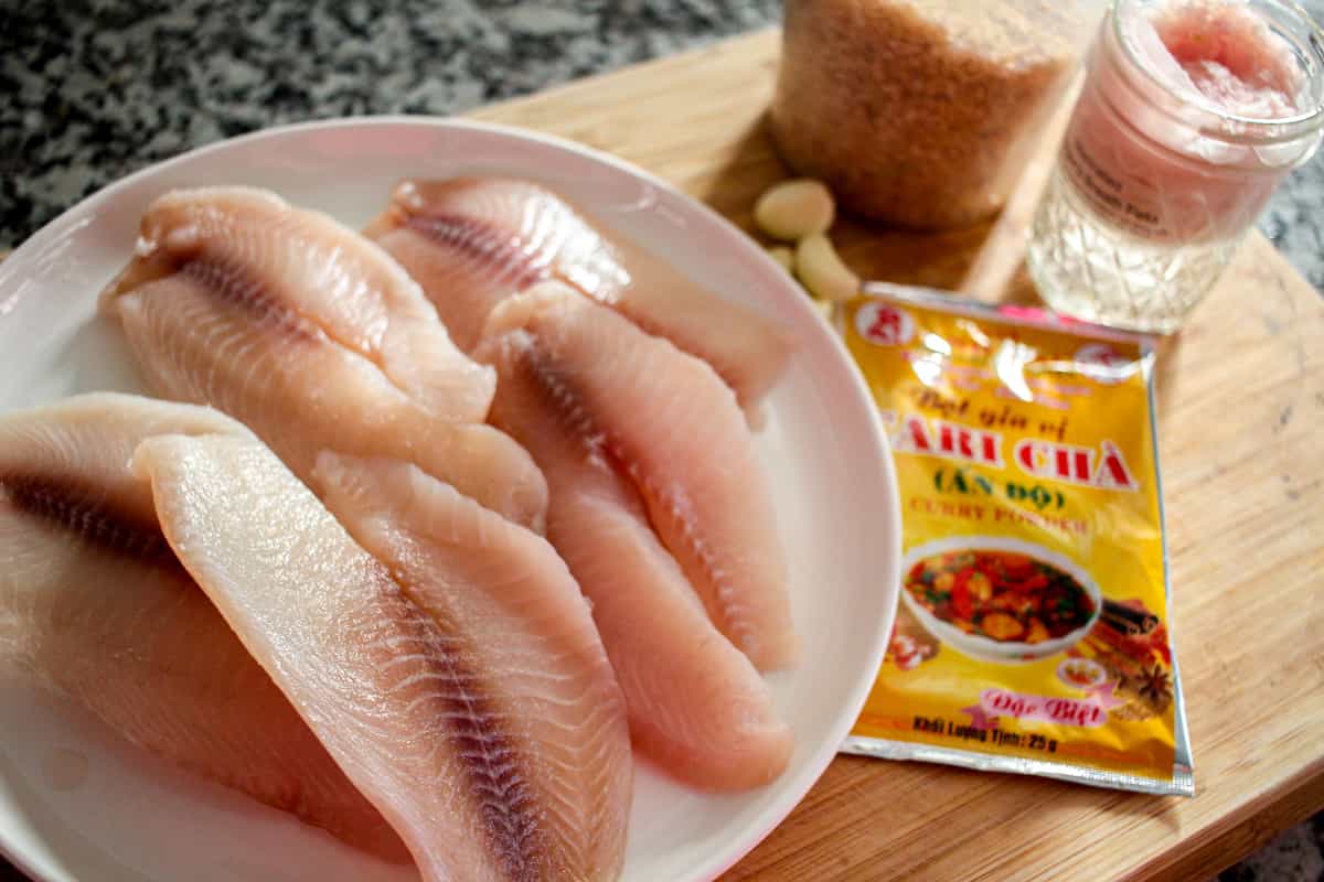 A wooden cutting board with a white plate of fish filets.