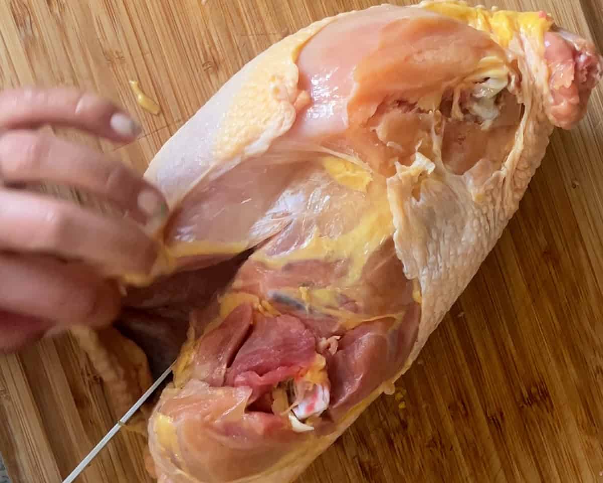 A hand with a knife cuts into a chicken carcass