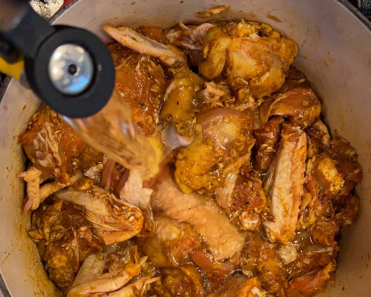 A spout pours water into a pot of marinated chicken