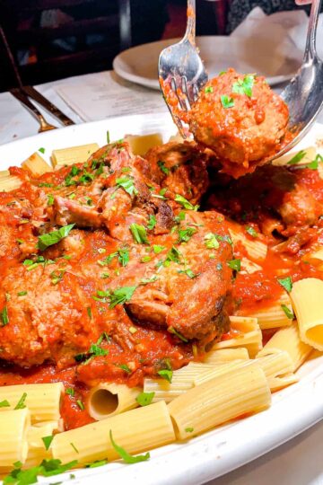 a large plate of rigatoni ragu, with a fork and spoon holding up a meatball in the upper right hand corner, from Carmine's