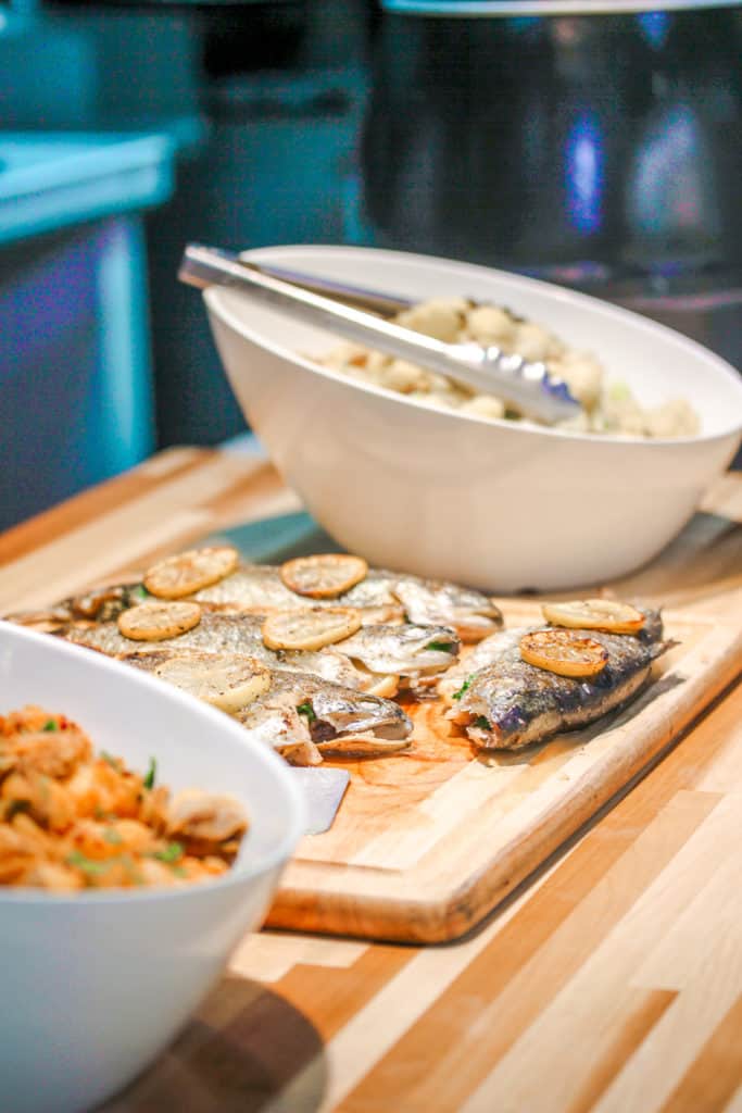 grilled fish between two white bowls with spicy potatoes and cauliflower