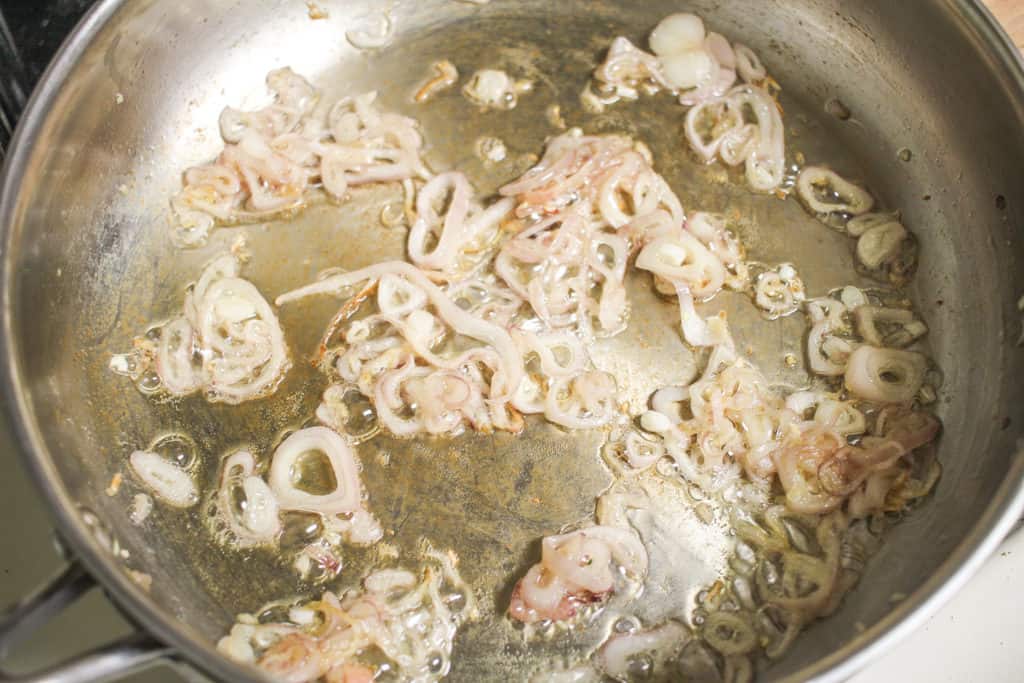 thinly sliced shallots in a stainless steel pan caramelizing