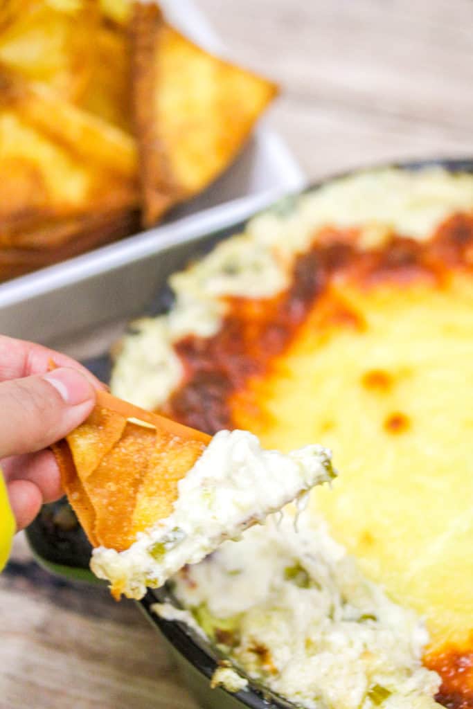 woman's hand holding a wonton chip with crab rangoon dip on it