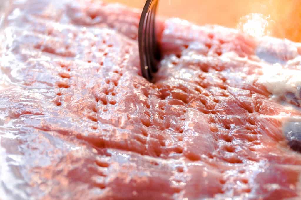 fork poking holes into the underside of pork belly