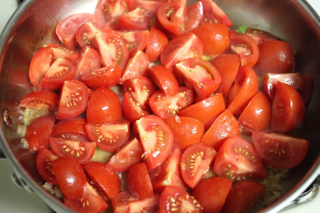 tomato wedges cooking in a stainless steel pan.