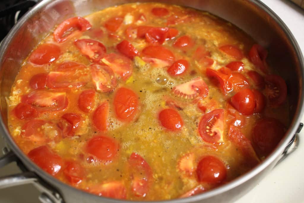 raw eggs in a pan full of tomato wedges