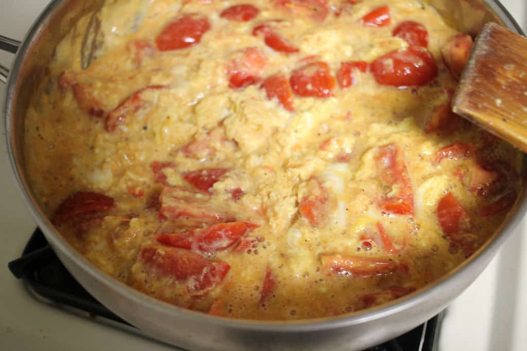 cooked eggs in a stainless steel pan full of tomato wedges