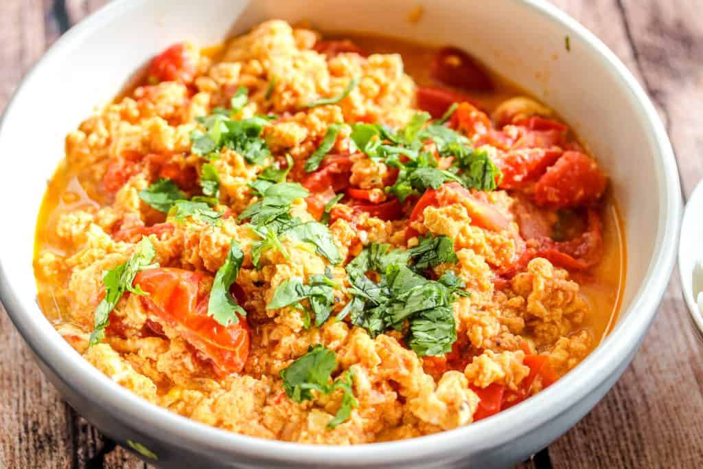 Egg and Tomato Stir fry in a blue bowl with cilantro sprinked on top