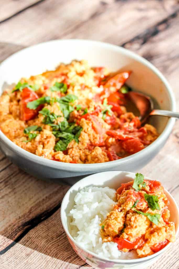 a small bowl of rice topped with eggs scrambled with tomatoes, sprinkled with cilantro. A bigger bowl of just the egg dish is in the background.