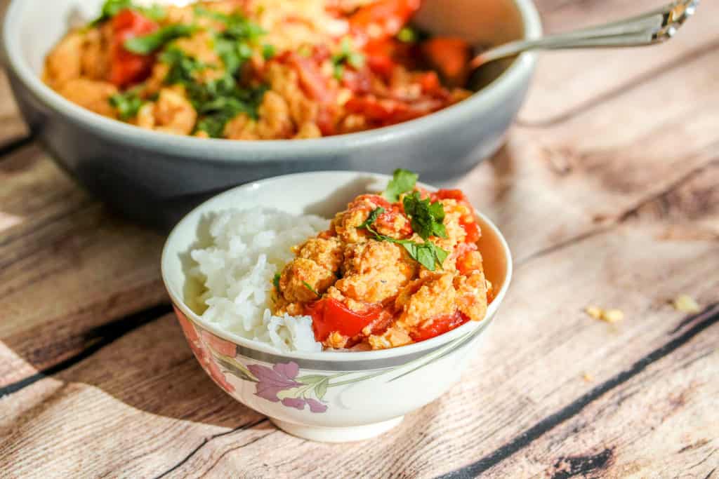 a small bowl of rice topped with eggs scrambled with tomatoes, sprinkled with cilantro. A bigger bowl of just the egg dish is in the background.