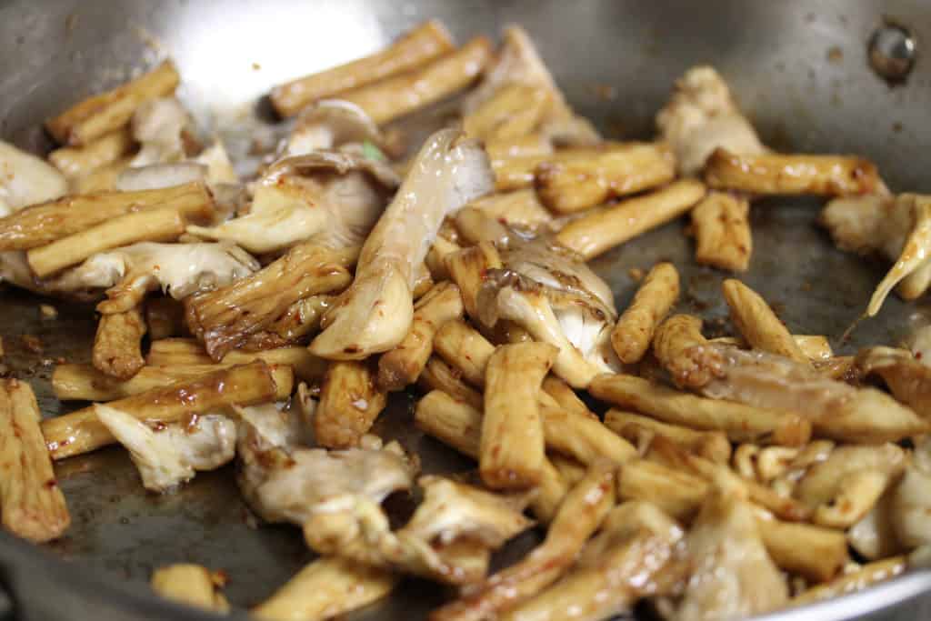 oyster mushrooms and tofu skin in a stainless steel pan, covered in oyster sauce.