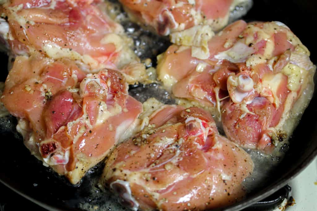 chicken thighs cooking skin side down in a cast iron skillet