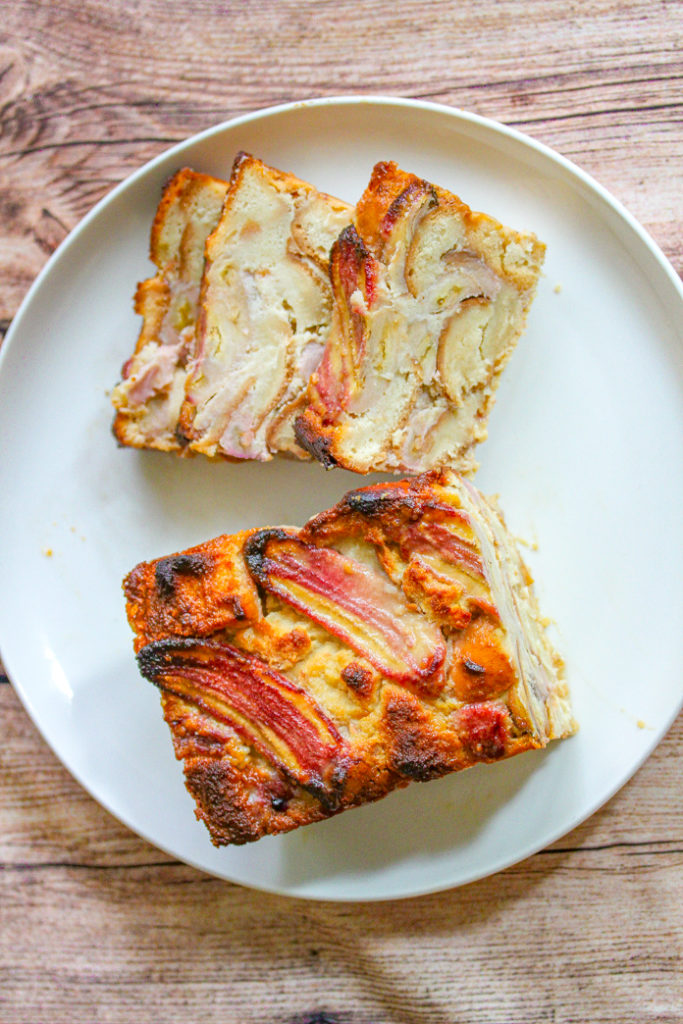 Half a loaf of banana bread with three slices of banana bread placed above it on a round white plate