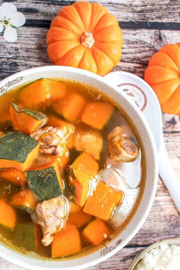 A birds eye view of a bowl of kabocha squash soup next to a spoon and two small pumpkins