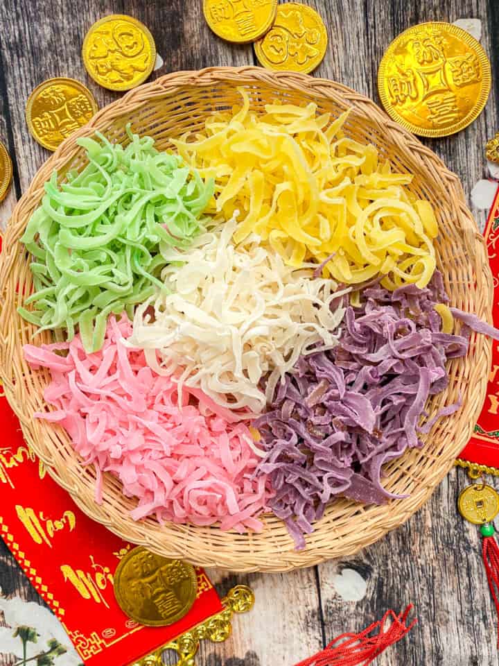 green, yellow, pink, purple and white Mứt Dừa, or coconut candy, on a wicker plate with lunar new year signs around it