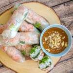 Shrimp and pork spring rolls (gỏi cuốn) on a round wooden board with a blue bowl filled with peanut sauce