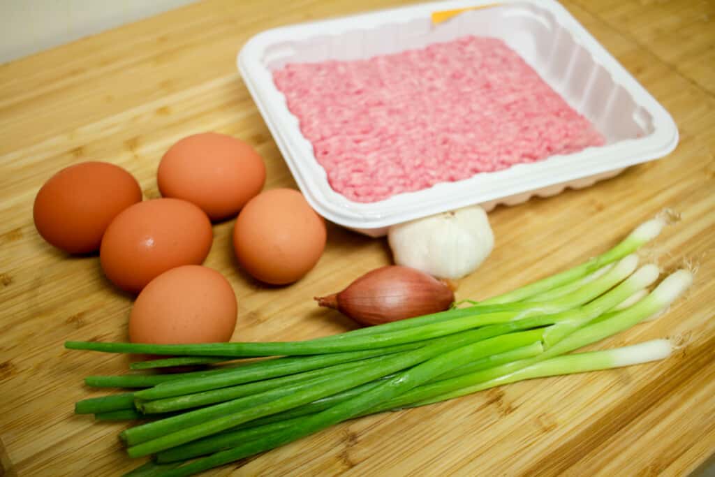 Eggs, ground pork, garlic, shallot and green onions on a wooden board