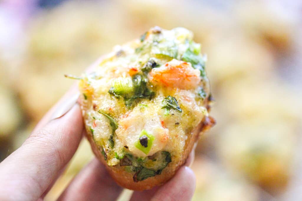 A closeup of a hand holding up a single piece of cooked shrimp toast