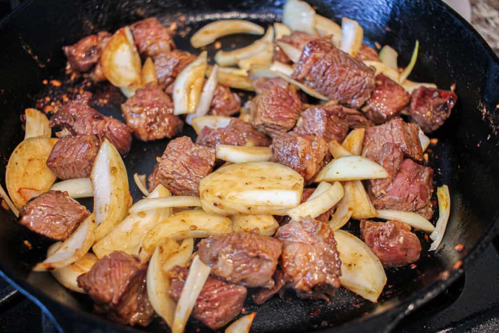 beef cubes and onions cooking in a cast iron skillet