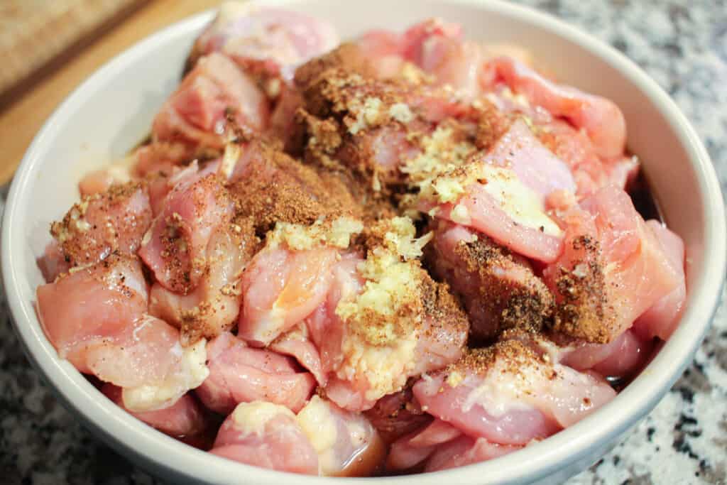 chicken thigh pieces in a ceramic bowl. The chicken is sprinkled with spices and fresh garlic and ginger