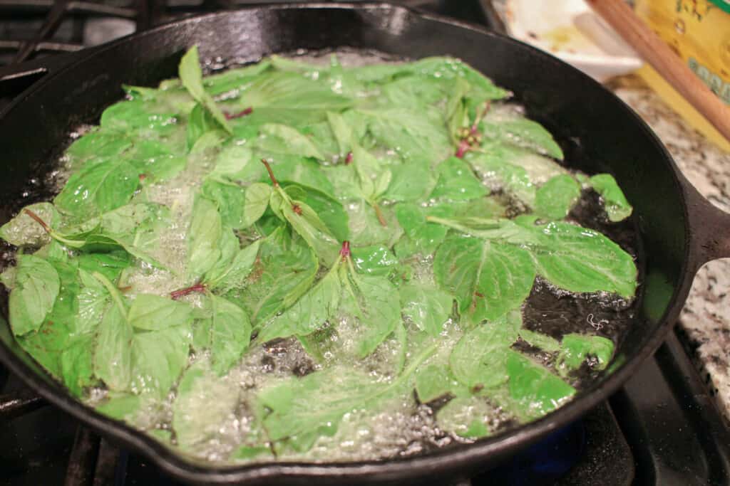 fresh thai basil leaves are deep frying in a cast iron skillet
