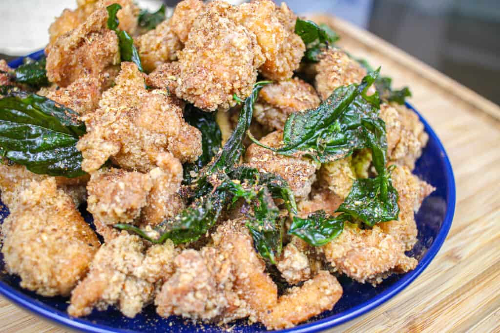 a pile of crispy taiwanese popcorn chicken pieces with deep fried basil leaves