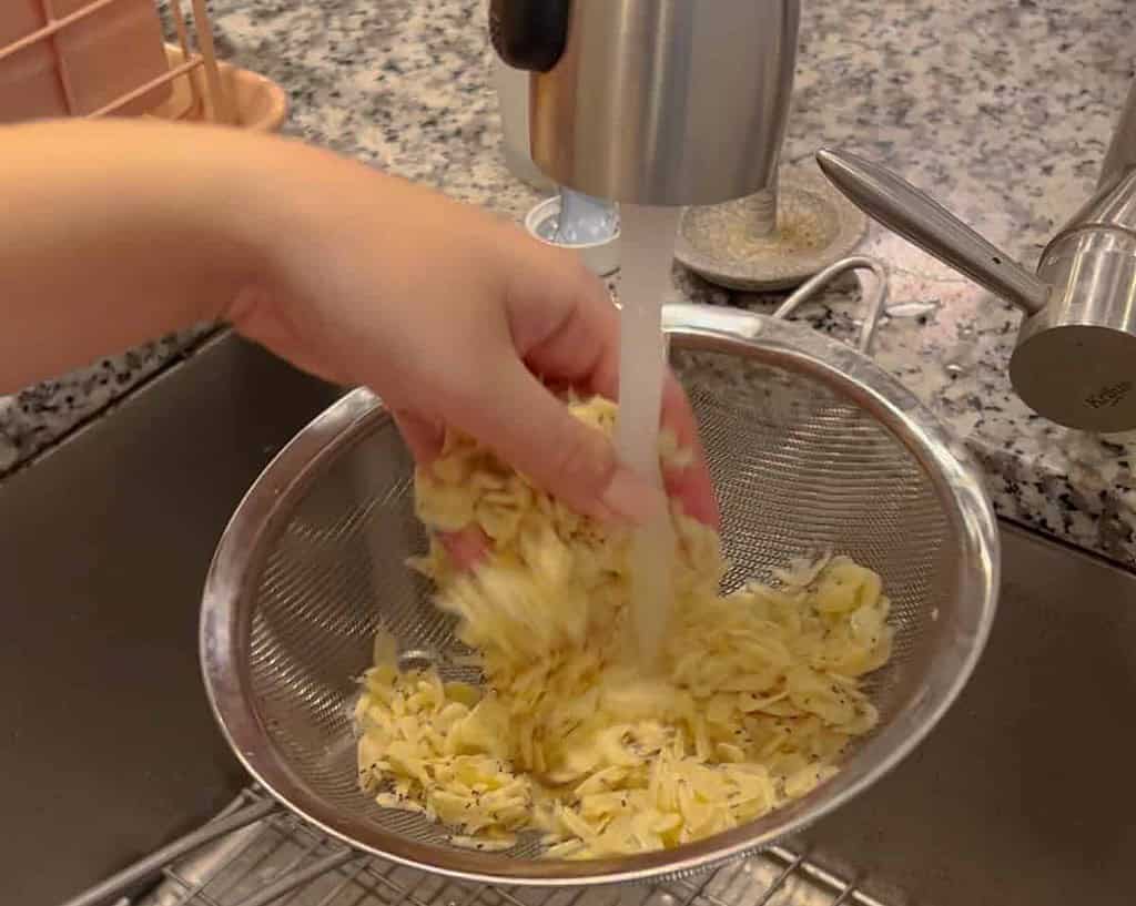 a metal strainer with tiny dried shrimp underneath a running faucet