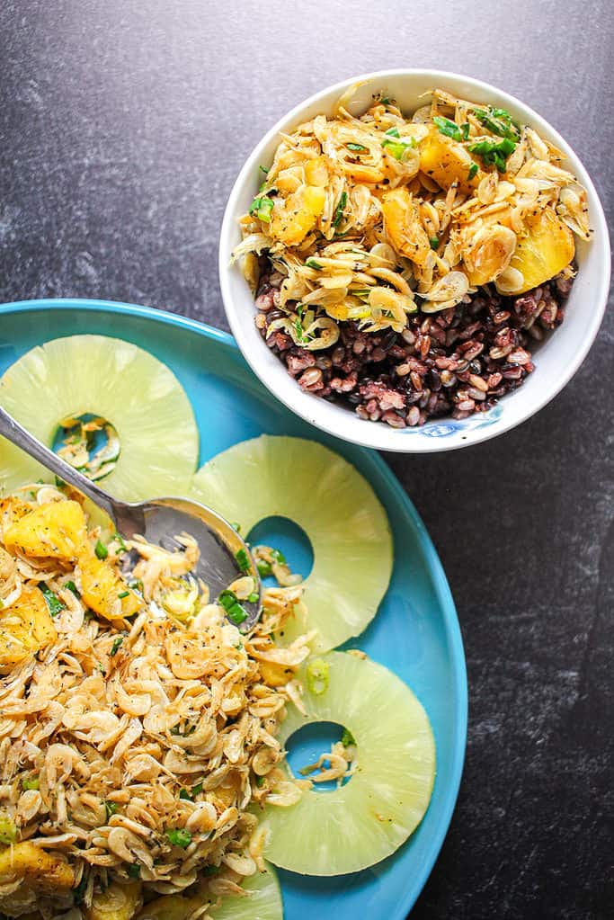 A small bowl of multigrain rice and dried shrimp with pineapple stir fry next to a larger plate of the same stir fry