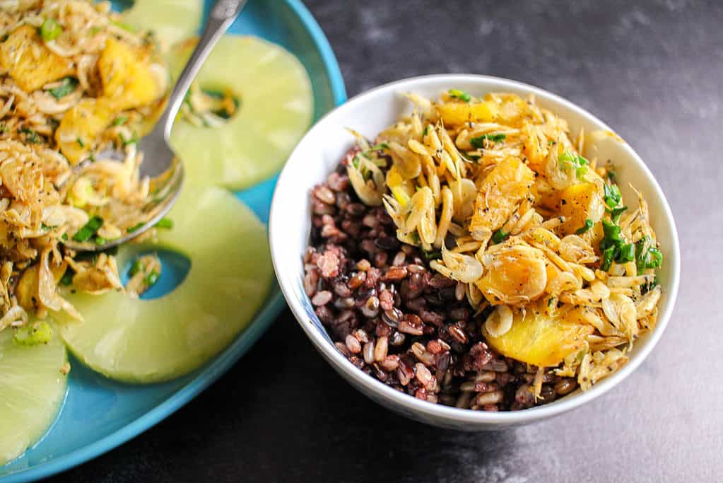 A close up of A small bowl of multigrain rice and dried shrimp with pineapple stir fry next to a larger plate of the same stir fry