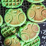 A square crop of a photo of three frog shaped coconut pandan waffles (Bánh Kẹp Lá Dứa) on a wire rack.