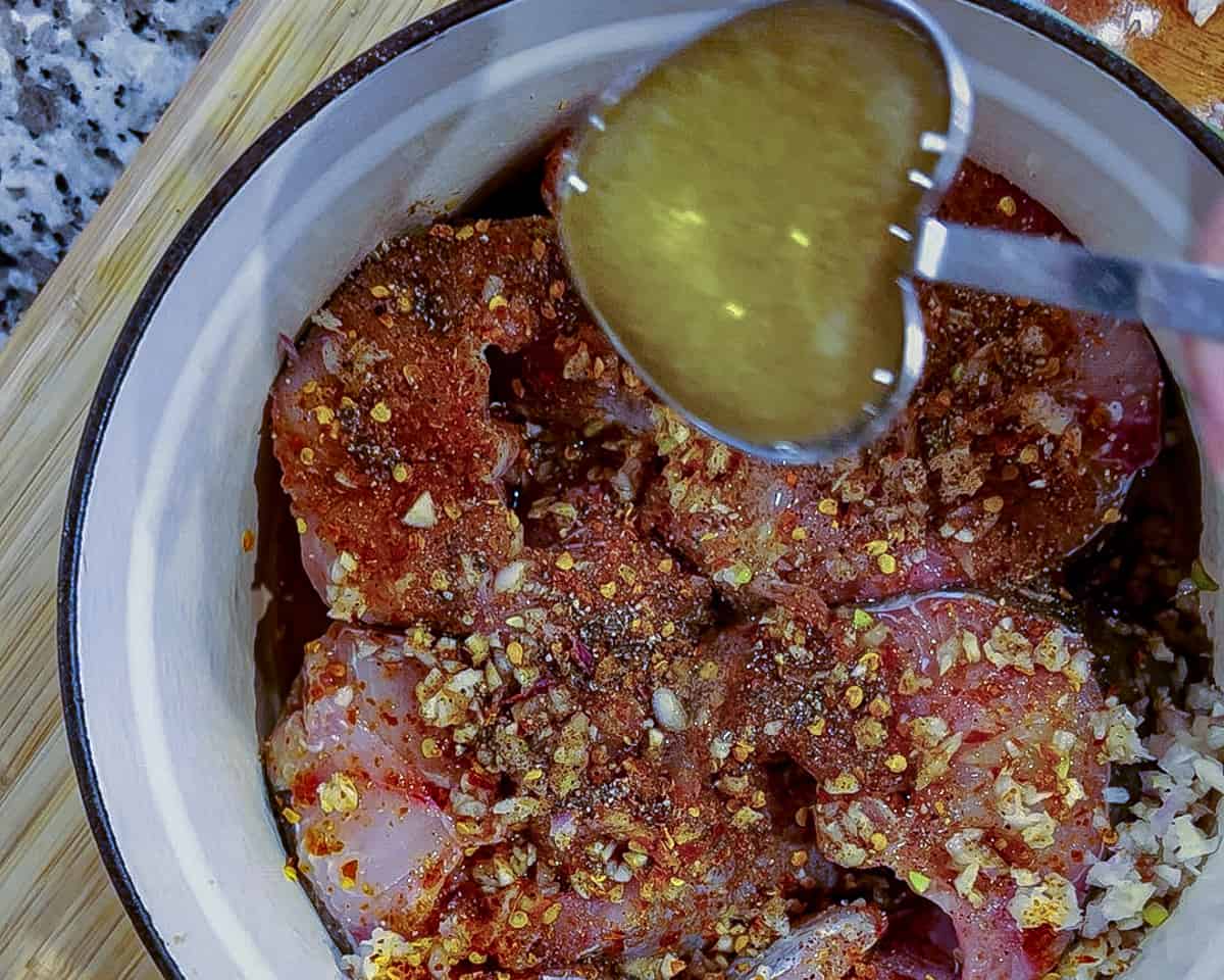 A heart shaped tablespoon filled with oil is drizzled over raw catfish steaks in a dutch oven