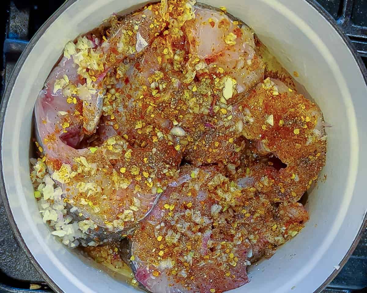 Raw catfish steaks topped with garlic, shallot, salt, pepper, chili flakes and oil in a dutch oven