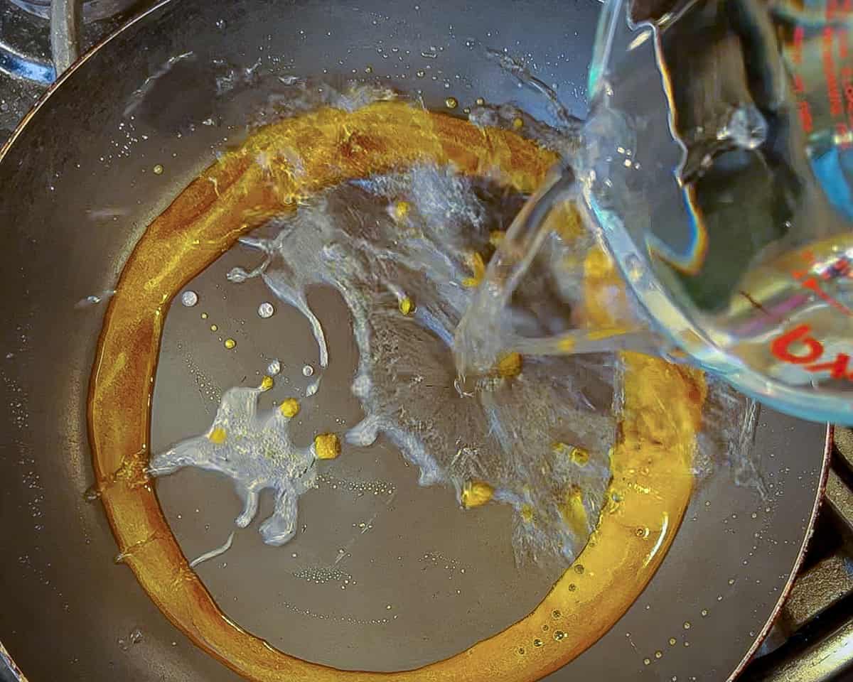 Water being poured into a nonstick pan full of caramelized sugar