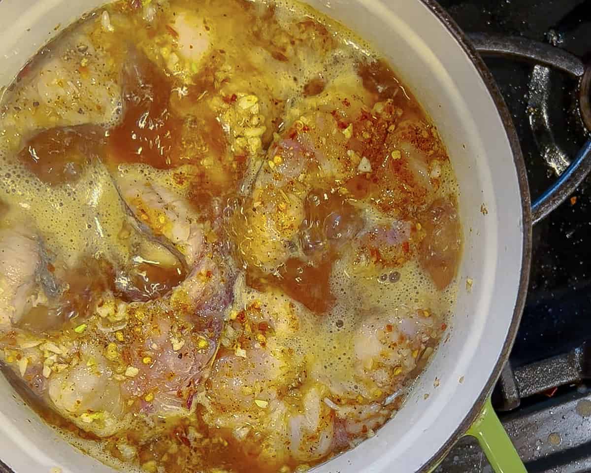 Catfish steaks simmering in a brown liquid in a dutch oven