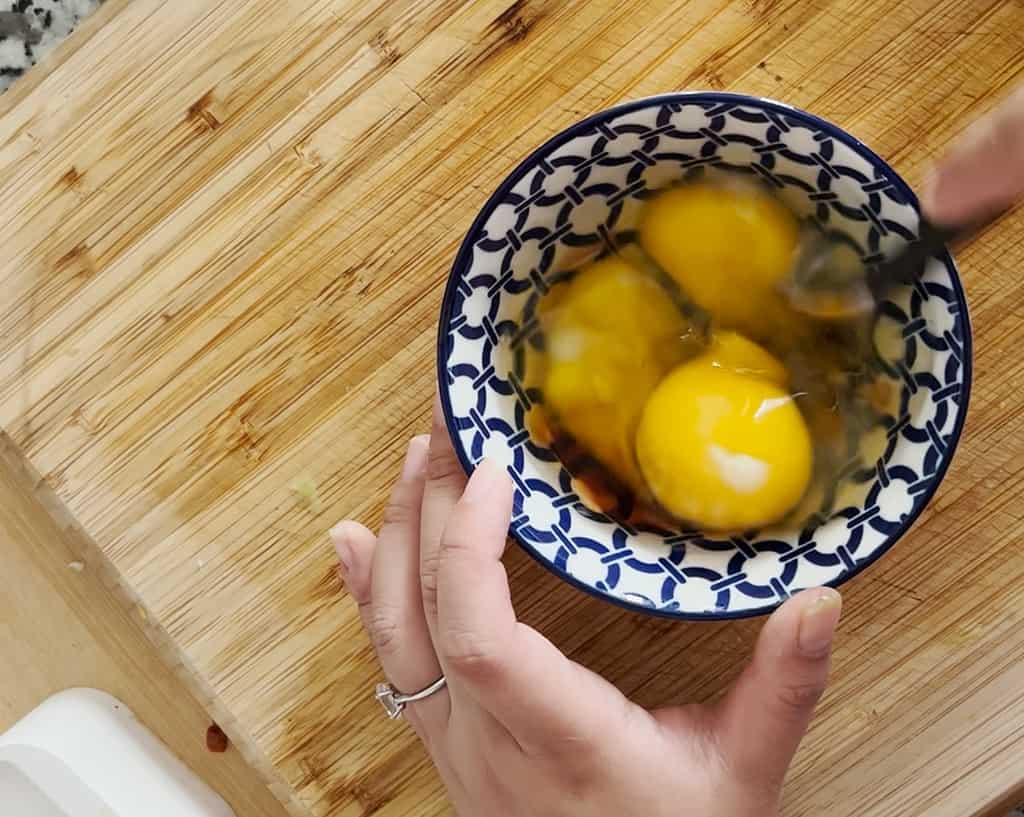 A hand uses a fork to beat three eggs with fish sauce