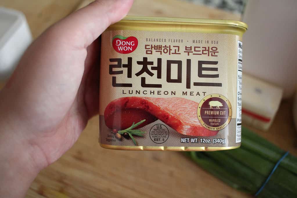 A hand holds up a can of Dong Won brand luncheon meat.