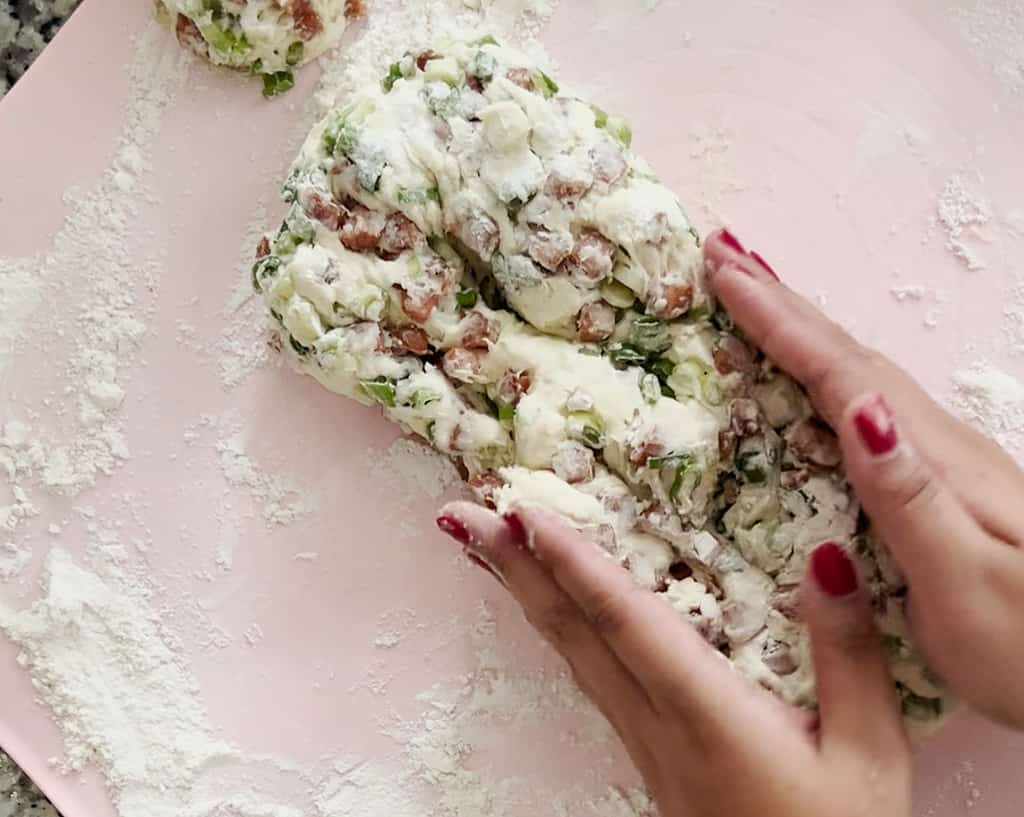 A bird's eye view of two hands smushing together spam and scallion biscuit dough