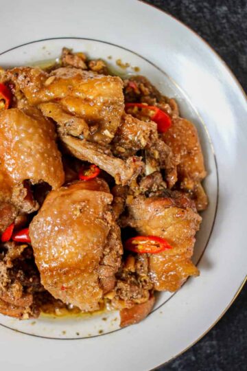 a square crop of a birds eye view of a bowl of ginger-braised chicken on a black background.