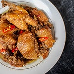 a square crop of a birds eye view of a bowl of ginger-braised chicken on a black background.