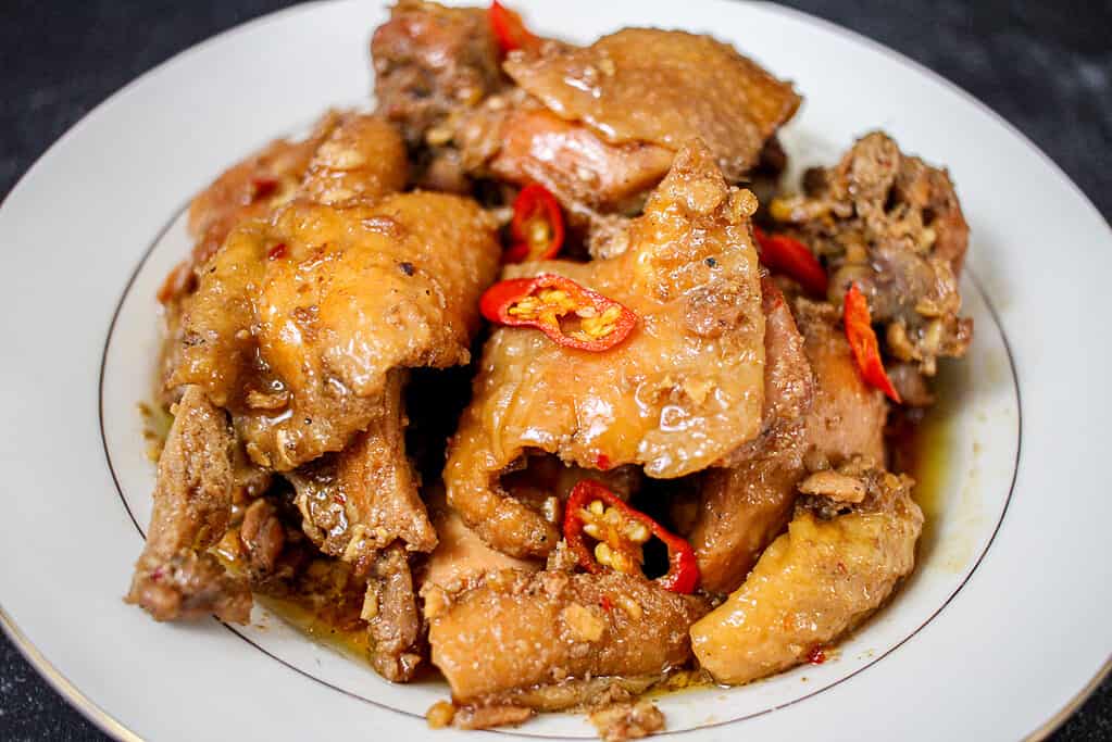 A white bowl with a gold rim sits on a black background. The bowl is filled with ginger-braised chicken.