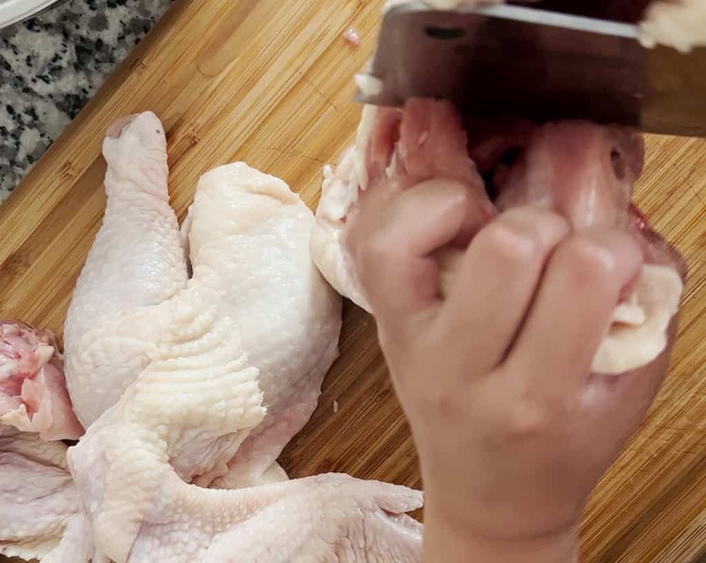 A hand uses a cleaver to chop up a chicken brease.