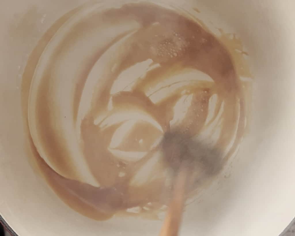 A wooden spatula stirs caramelized sugar in a dutch oven