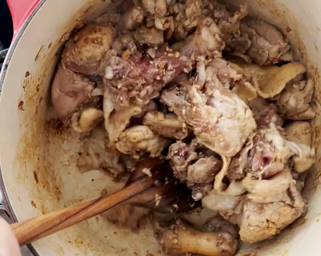 A wooden spoon stirs chicken in a dutch oven