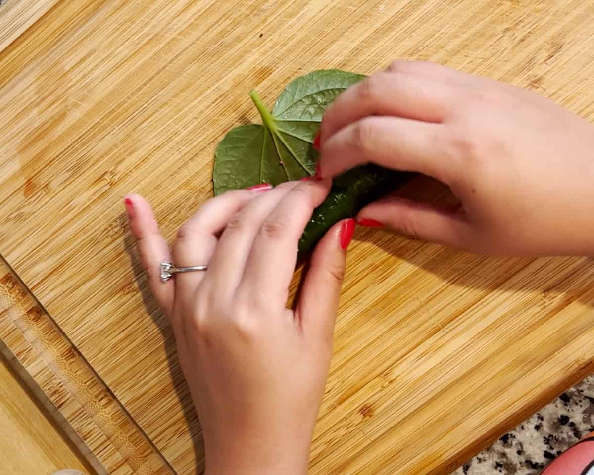 Two hands roll up a small log of marinated ground beef inside of a betel leaf.