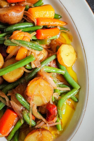 A plate of Vietnamese potato salad, which consists of potatoes, green beans, shallots, carrots and vinaigrette, on a plate on a table.