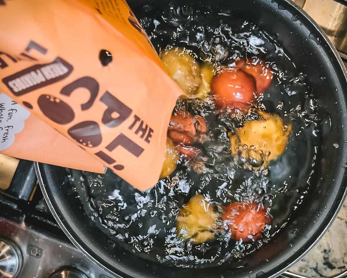 A bag of potatoes being poured into a pot of boiling water.