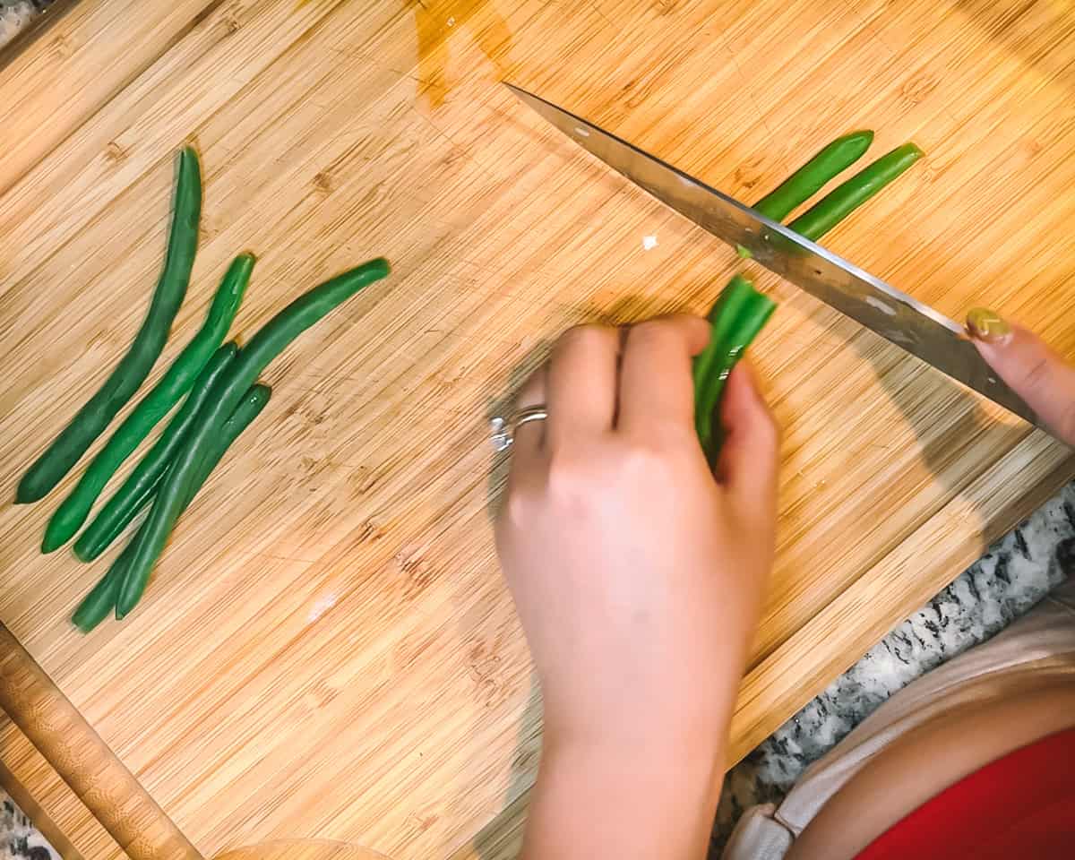 Two hands cut up green beans on a wooden board