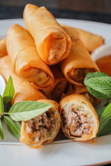 Plated Vietnamese fried spring rolls with fresh herbs and dipping sauce, close-up on texture and filling.