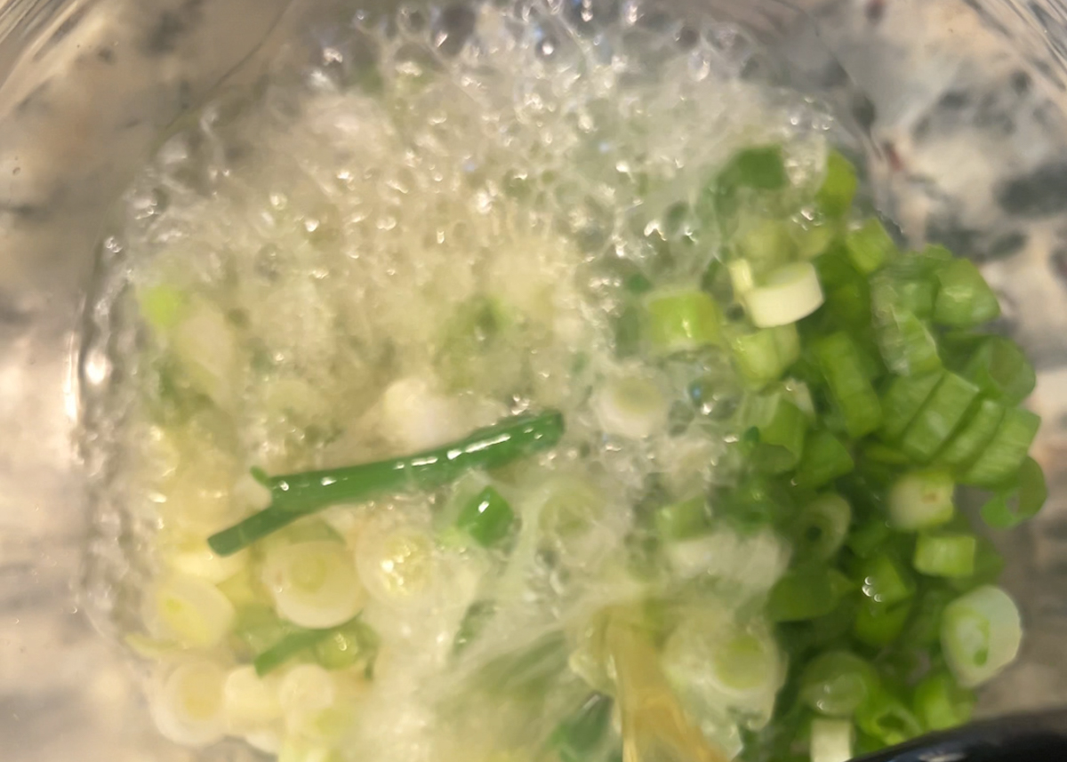 hot oil sizzing in a clear bowl filled with chopped scallions