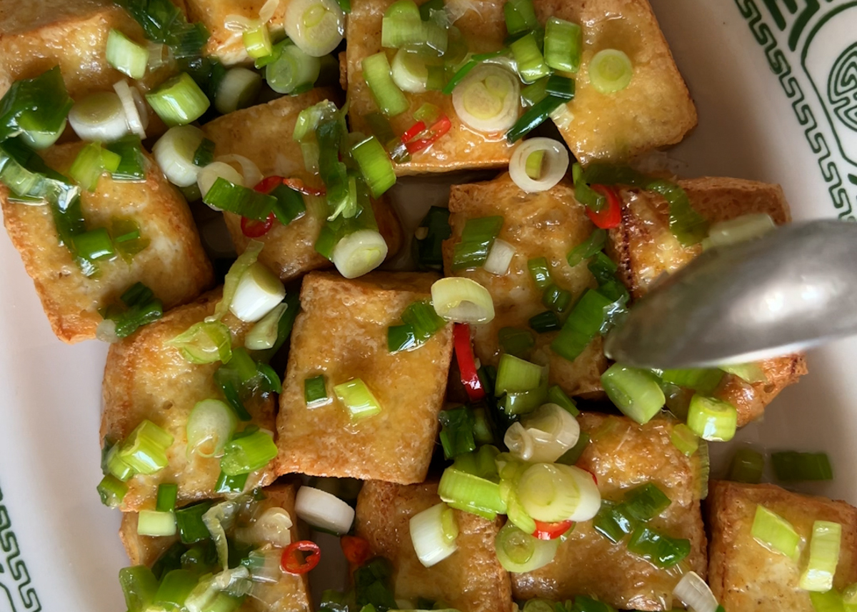 A hand spoons scallion oil over fried tofu